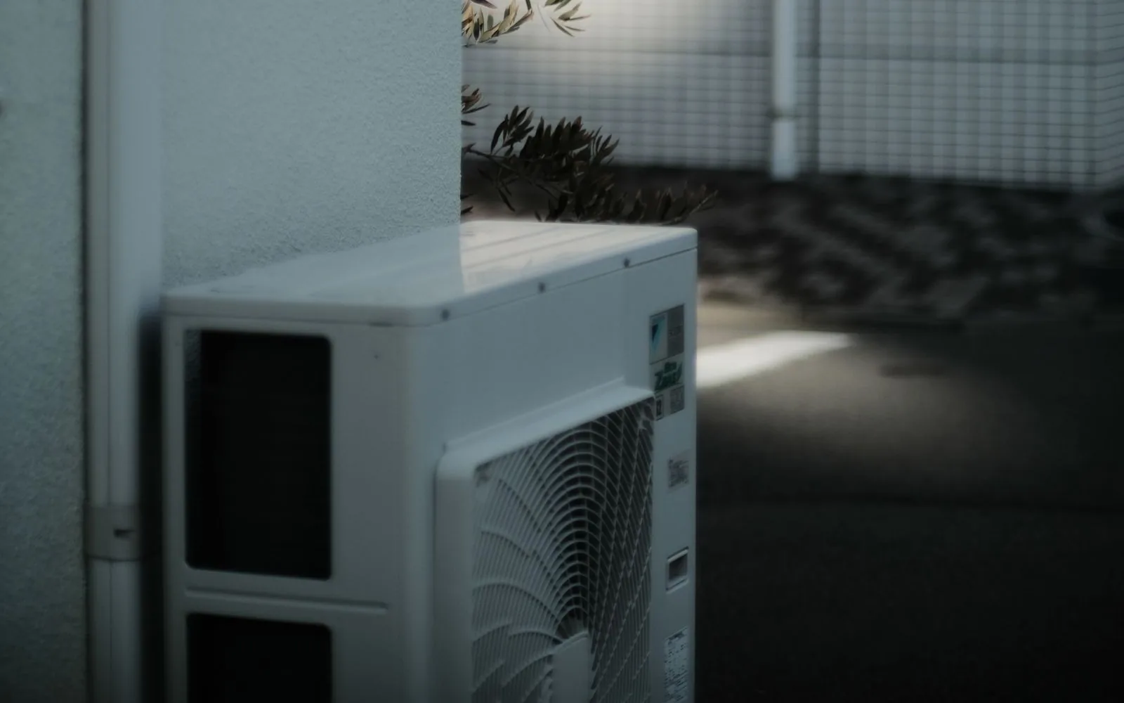 Outdoor air conditioning condenser beside a white exterior wall